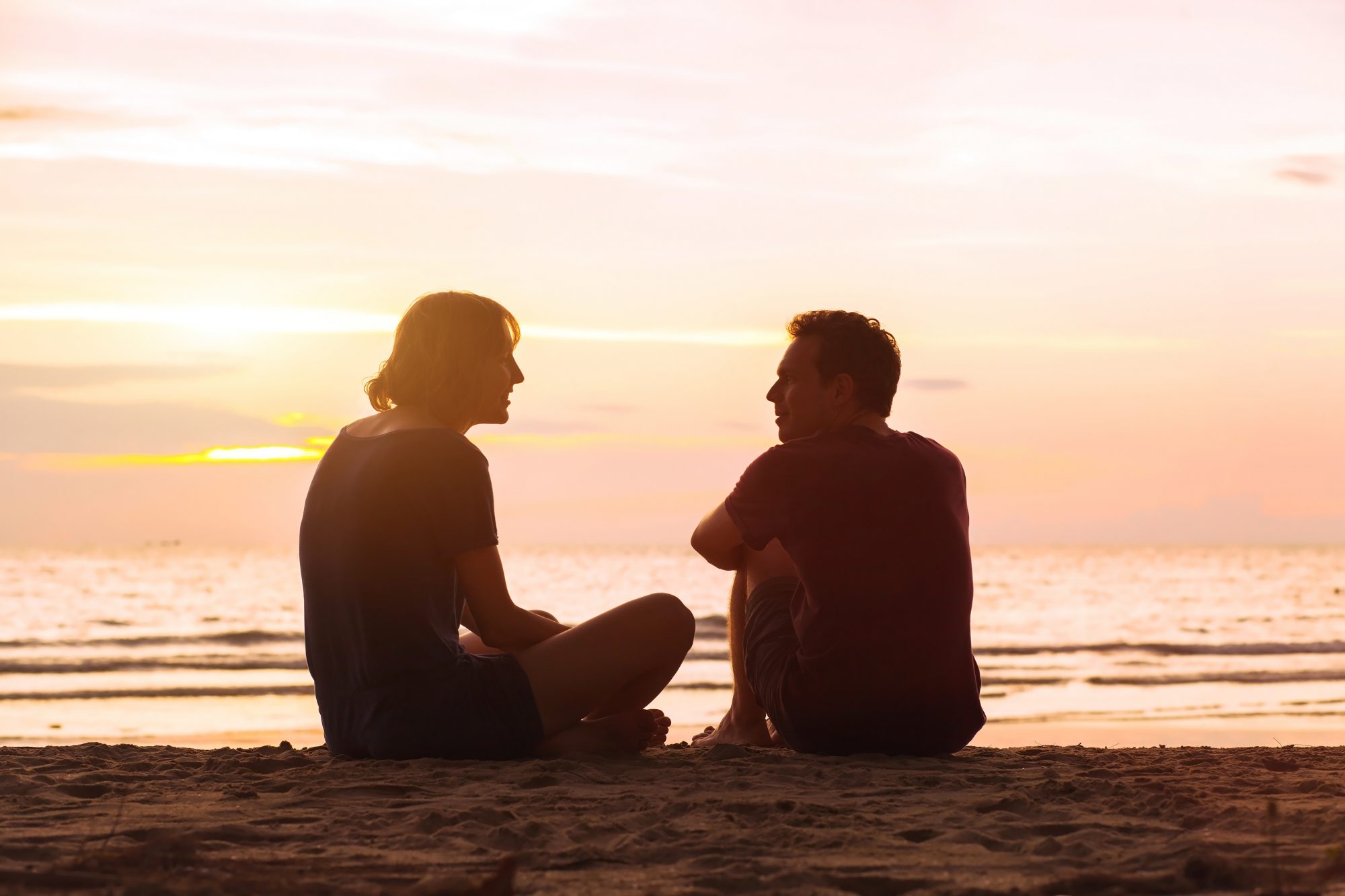 man and woman on the beach at sunset, young couple talking near the sea, dating or friendship concept