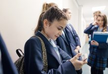 A group of students waiting in line in a school corridor, one is checking her phone