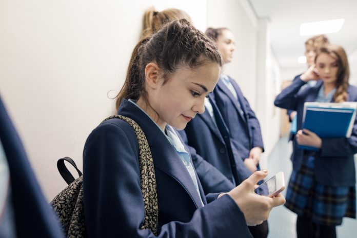 A group of students waiting in line in a school corridor, one is checking her phone