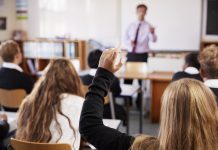 Female Student Raising Hand To Ask Question In Classroom