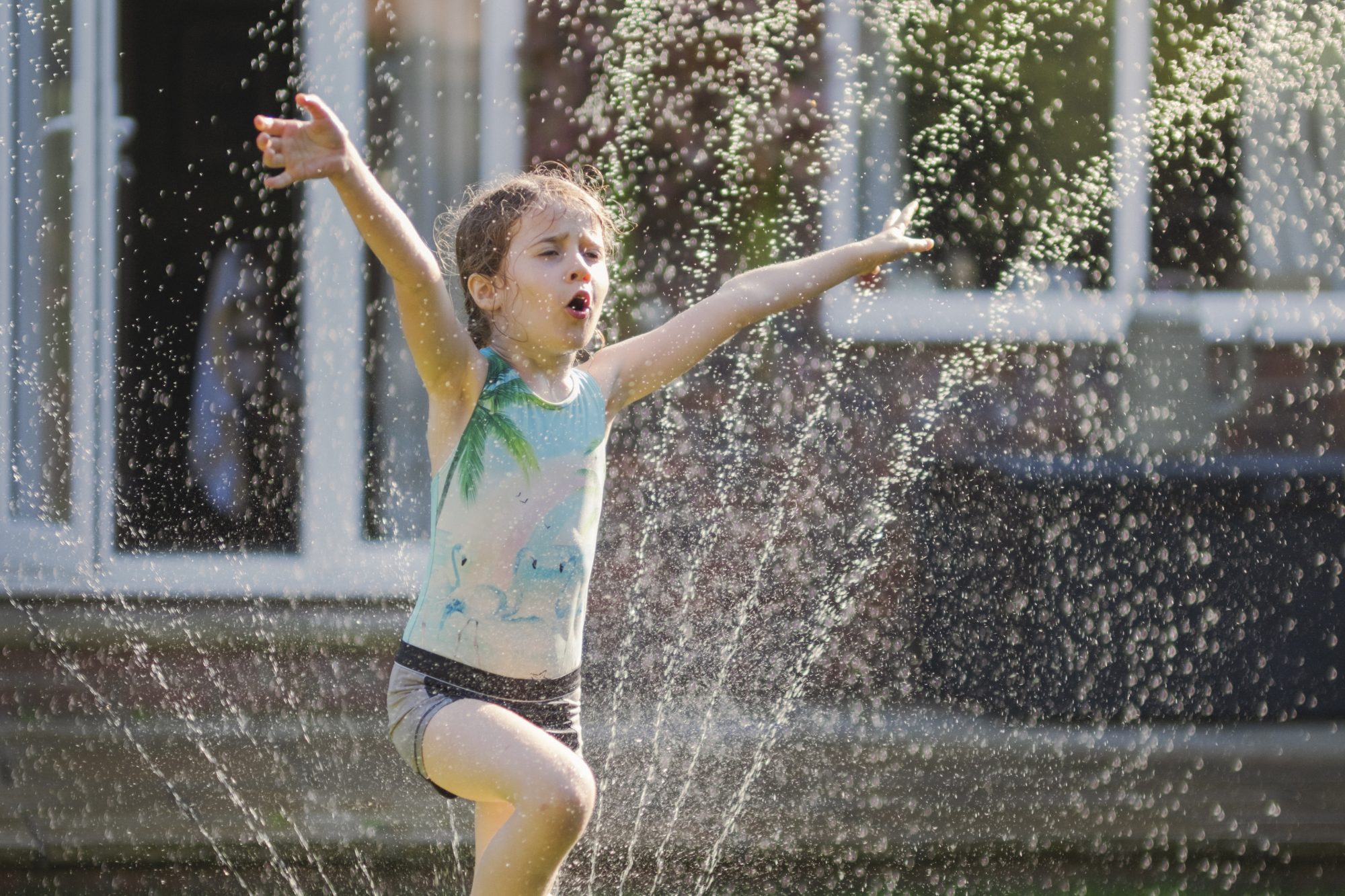 A happy girl is jumping through a sprinkler