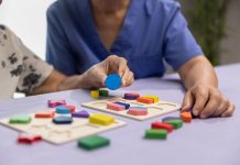 Caregiver and senior woman playing wooden shape puzzles game for dementia prevention