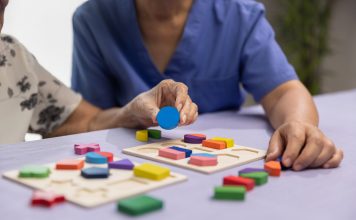 Caregiver and senior woman playing wooden shape puzzles game for dementia prevention