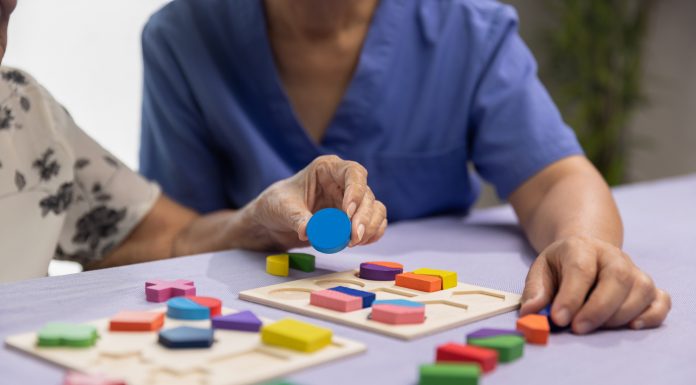 Caregiver and senior woman playing wooden shape puzzles game for dementia prevention