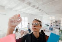 Photo of a young woman writing on a transparent wipe board and thinking of a solution for her work-related problems