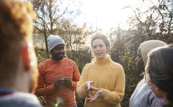 A multiracial group of volunteers wearing warm casual clothing and accessories on a sunny cold winters day. They are talking before they start working on a community farm, planting trees and performing other tasks.