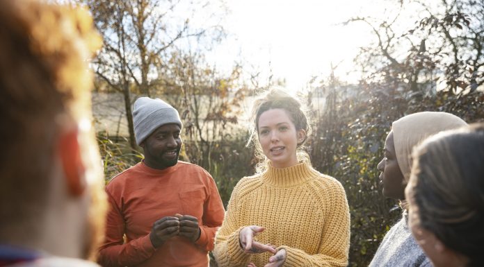 A multiracial group of volunteers wearing warm casual clothing and accessories on a sunny cold winters day. They are talking before they start working on a community farm, planting trees and performing other tasks.