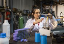 A medium close up view of a female mechanic working in a garage and recycling lithium batteries she is using hazardous materials and is using laboratory glassware for her work. She is also using an electric hotplate stirrer in the process of recycling.