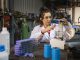 A medium close up view of a female mechanic working in a garage and recycling lithium batteries she is using hazardous materials and is using laboratory glassware for her work. She is also using an electric hotplate stirrer in the process of recycling.