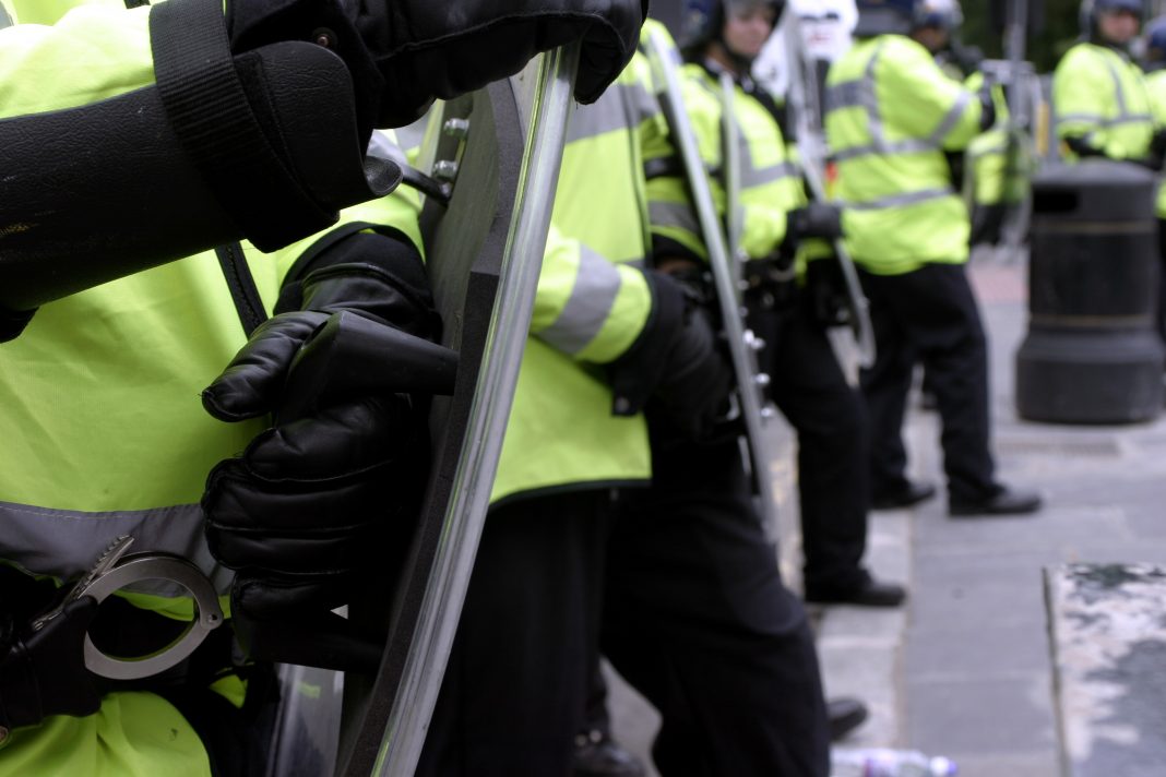British police officers in riot gear form a human wall during a demonstration.
