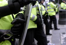 British police officers in riot gear form a human wall during a demonstration.