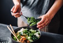 Close-up of woman eating omega 3 rich salad. Female having healthy salad consist of chopped salmon, spinach, brussels sprouts, avocado, soybeans, wakame and chia seeds in a bowl.