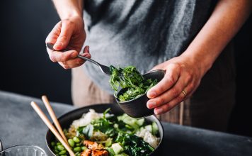 Close-up of woman eating omega 3 rich salad. Female having healthy salad consist of chopped salmon, spinach, brussels sprouts, avocado, soybeans, wakame and chia seeds in a bowl.