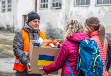 Volunteer in orange west gives a box of food donation to fleeing refugees from Ukraine.