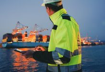 Man in protective gear holding tablet computer in front of harbor terminal at night