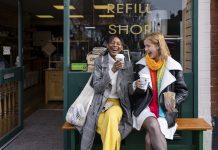 Two friends sitting outside a store that promotes sustainable living in the North East of England. The store has refill stations to reduce plastic and food waste. The store sells homemade organic bars of soap as well as vegan based foods.