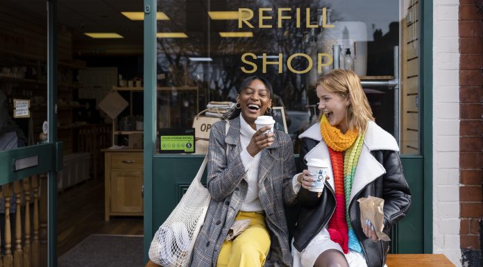 Two friends sitting outside a store that promotes sustainable living in the North East of England. The store has refill stations to reduce plastic and food waste. The store sells homemade organic bars of soap as well as vegan based foods.