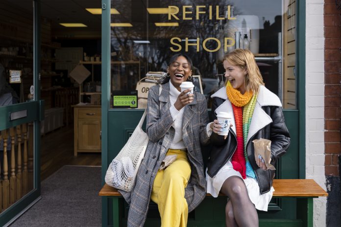 Two friends sitting outside a store that promotes sustainable living in the North East of England. The store has refill stations to reduce plastic and food waste. The store sells homemade organic bars of soap as well as vegan based foods.