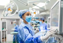 Anesthetist Working In Operating Theatre Wearing Protecive Gear checking monitors while sedating patient before surgical procedure in hospital