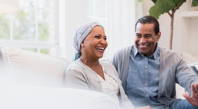 Sitting on their sofa at home, the senior adult couple smiles and laughs at a joke.