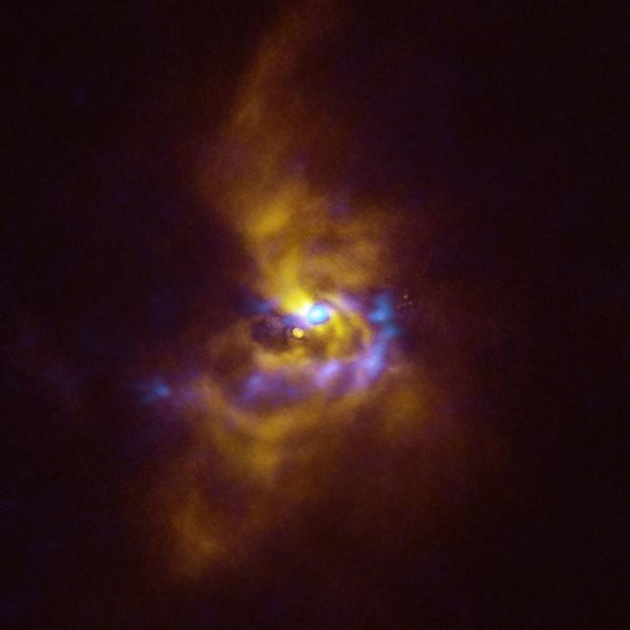 At the centre of this image is the young star V960 Mon, located over 5000 light-years away in the constellation Monoceros. Dusty material with potential to form planets surrounds the star.  Observations obtained using the Spectro-Polarimetric High-contrast Exoplanet REsearch (SPHERE) instrument on ESO’s VLT, represented in yellow in this image, show that the dusty material orbiting the young star is assembling together in a series of intricate spiral arms extending to distances greater than the entire Solar System.  Meanwhile, the blue regions represent data obtained with the Atacama Large Millimeter/submillimeter Array (ALMA), in which ESO is a partner. The ALMA data peers deeper into the structure of the spiral arms, revealing large dusty clumps that could contract and collapse to form giant planets roughly the size of Jupiter via a process known as “gravitational instability”.