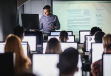 Mid adult professor teaching a lecture from desktop PC at computer lab.