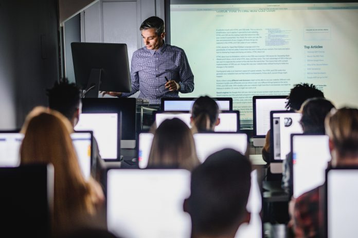 Mid adult professor teaching a lecture from desktop PC at computer lab.