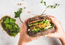 Vegan sandwich with chickpea patty, avocado, cucumber and greens in rye bread in children's hands.