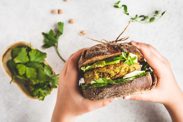 Vegan sandwich with chickpea patty, avocado, cucumber and greens in rye bread in children's hands.