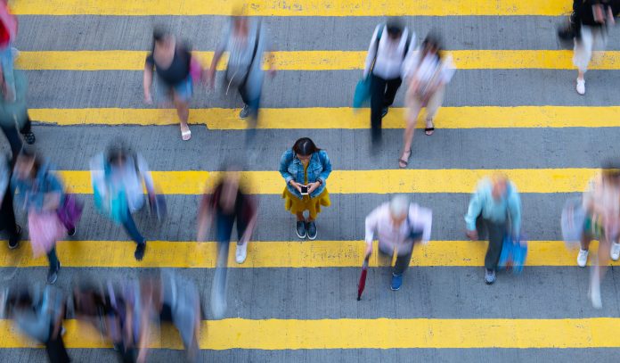 Young woman standing, with phone, in motion blurred crowd