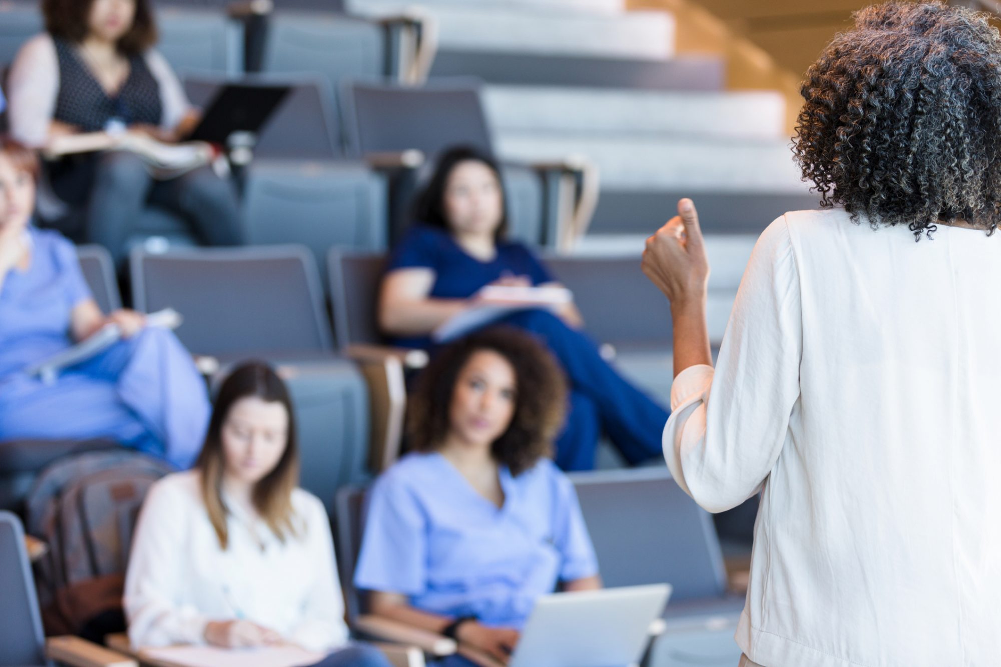 Unrecognizable teacher gestures as she lectures a class of students.