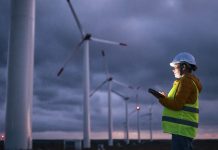 Renewable Energy Systems. Electricity Maintenance Engineer working on the field at a Wind Turbine Power station at dusk with a moody sky behind. Blurred motion.