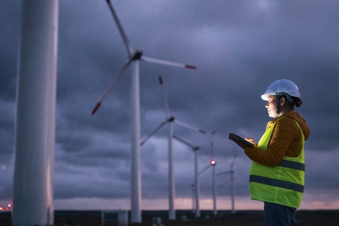 Renewable Energy Systems. Electricity Maintenance Engineer working on the field at a Wind Turbine Power station at dusk with a moody sky behind. Blurred motion.