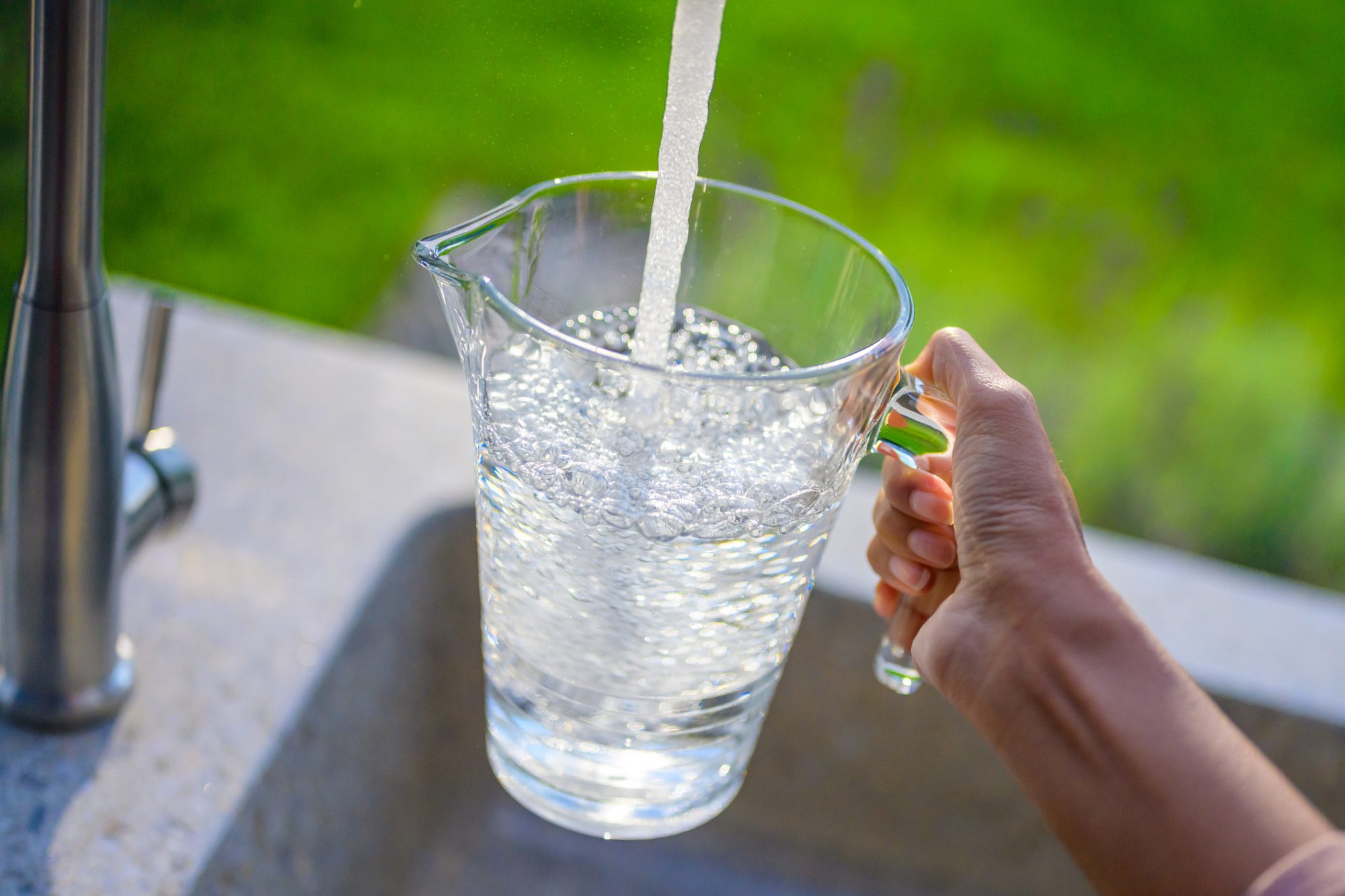 Close-up of woman's hand filling pitcher with water in garden sink.