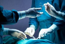 doctor and nurse medical team are performing surgical operation at emergency room in hospital. assistant hands out scissor and instruments to surgeons during operation.