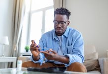 man is sitting at the sofa and taking blood from his finger due to diabetes. The daily life of a man of African-American ethnicity person with a chronic illness who is using glucose tester.