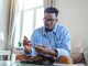 man is sitting at the sofa and taking blood from his finger due to diabetes. The daily life of a man of African-American ethnicity person with a chronic illness who is using glucose tester.