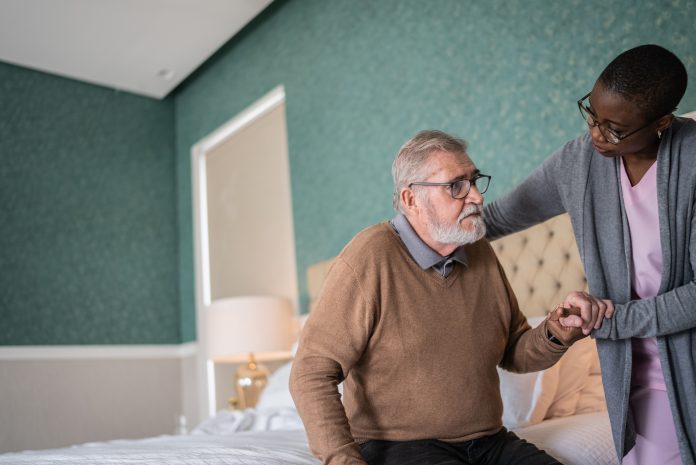 Home caregiver helping senior patient standing up in the bed