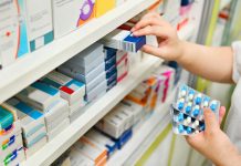 Pharmacist holding medicine box and capsule pack in pharmacy drugstore.