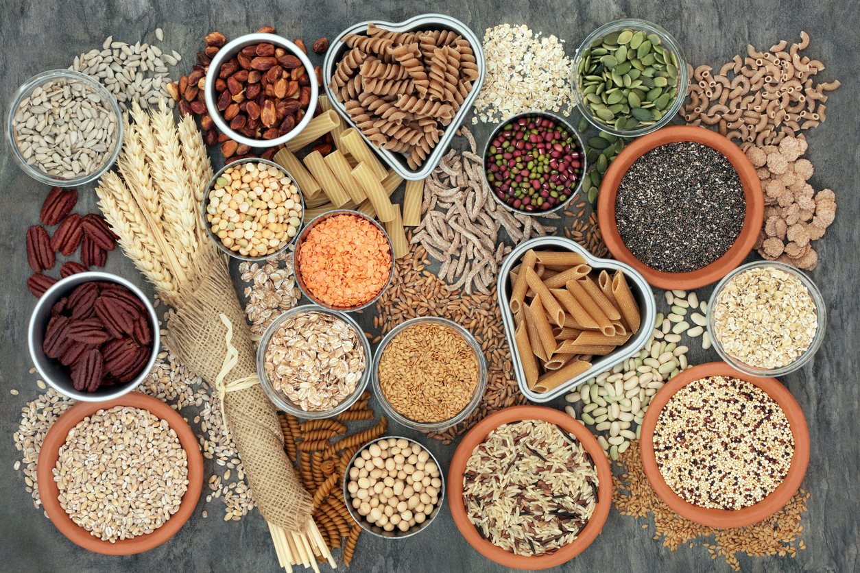 Healthy high fibre dietary food concept with whole wheat pasta, legumes, nuts, seeds, cereals, grains and wheat sheaths. High in omega 3, antioxidants, vitamins. On marble background top view.