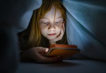 Girl using a mobile phone in the night. Kid skipping sleep hooked on the phone