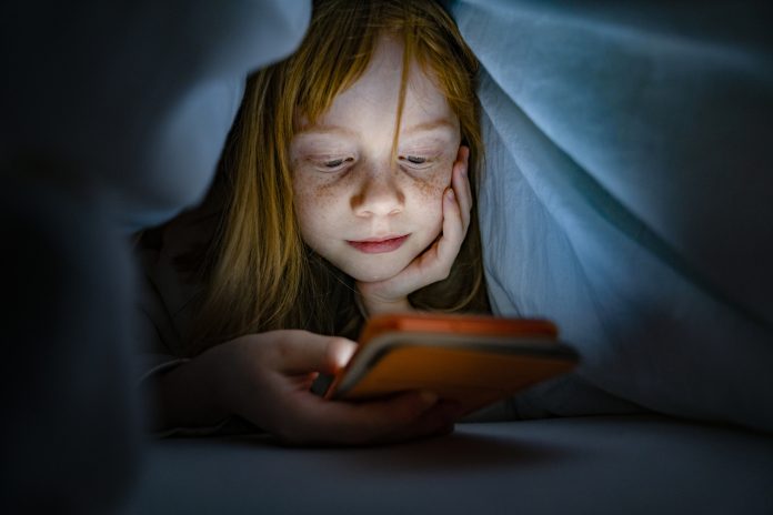 Girl using a mobile phone in the night. Kid skipping sleep hooked on the phone