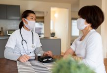 Nurse wearing a mask talking to an elderly patient during a home visit. Okayama, Japan, preventative care