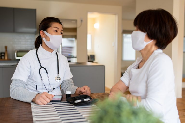 Nurse wearing a mask talking to an elderly patient during a home visit. Okayama, Japan, preventative care