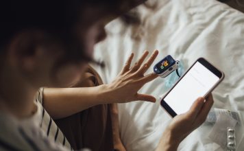 An anonymous Caucasian female reading some health articles on her mobile phone while using oximeter to check her blood condition.