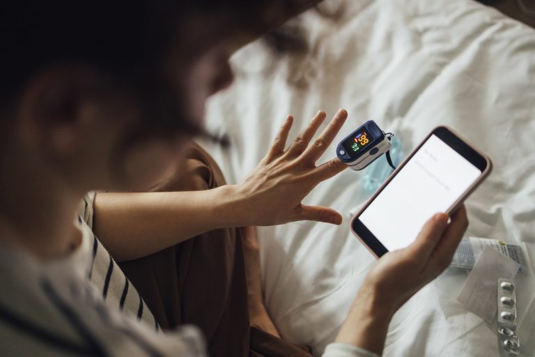 An anonymous Caucasian female reading some health articles on her mobile phone while using oximeter to check her blood condition.