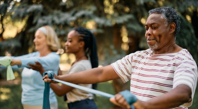 African American mature man practicing with power band on exercise class in nature.