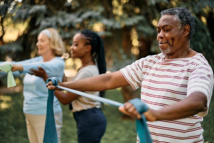 African American mature man practicing with power band on exercise class in nature.