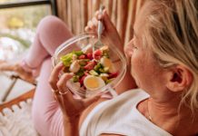 View of yummy vegetarian salad, woman sitting and relaxing on a chair, unrecognisable person view from above the shoulder