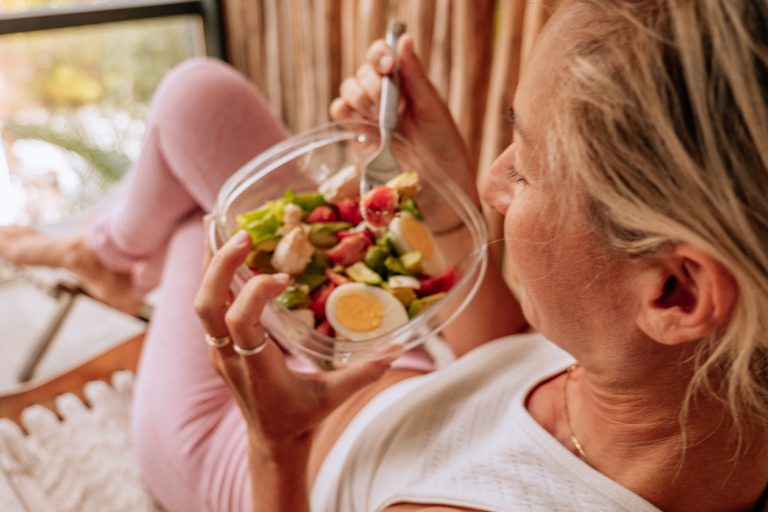 View of yummy vegetarian salad, woman sitting and relaxing on a chair, unrecognisable person view from above the shoulder